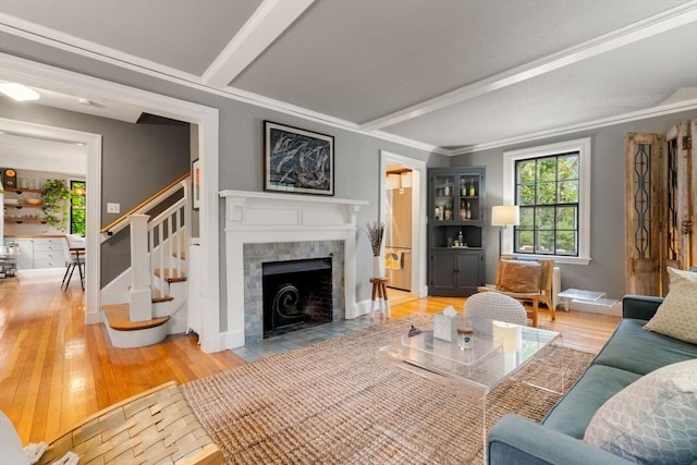 living area with stairs, ornamental molding, a tiled fireplace, and wood finished floors