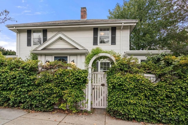 traditional-style home featuring a fenced front yard, a gate, and a chimney