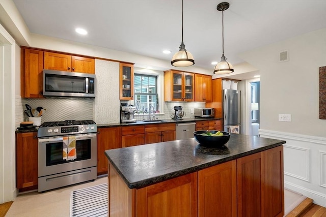 kitchen featuring dark countertops, appliances with stainless steel finishes, brown cabinets, and wainscoting