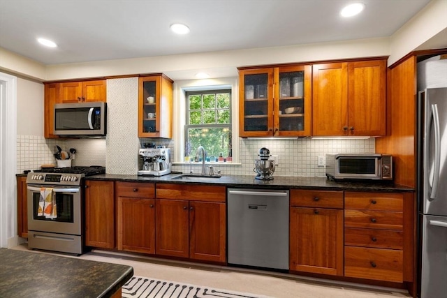 kitchen with a toaster, a sink, appliances with stainless steel finishes, brown cabinets, and dark stone counters