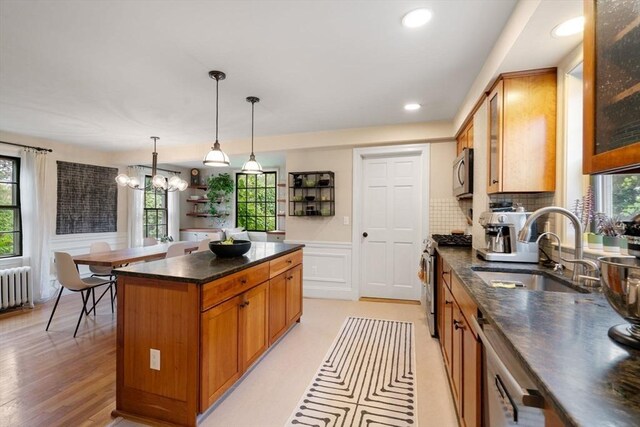 kitchen with stainless steel appliances, radiator heating unit, brown cabinetry, wainscoting, and a sink