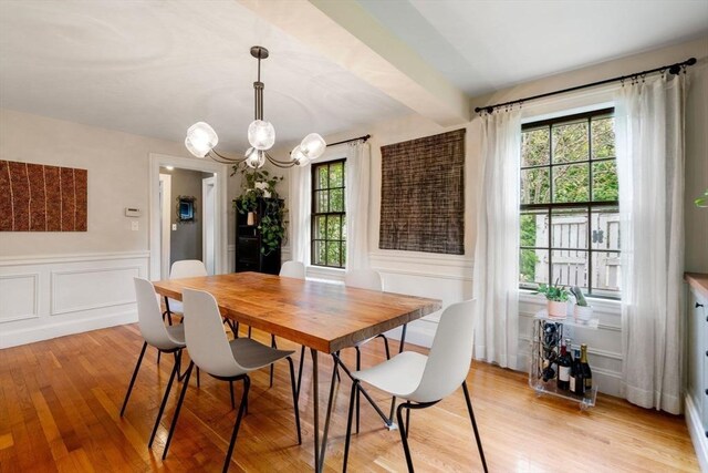 dining area featuring a decorative wall, an inviting chandelier, wainscoting, light wood-type flooring, and beamed ceiling