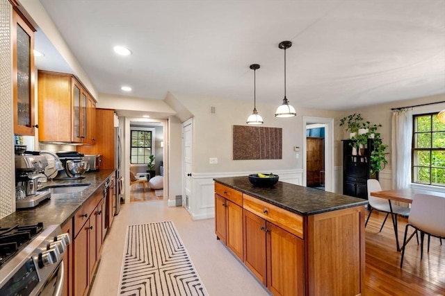 kitchen with a wainscoted wall, glass insert cabinets, appliances with stainless steel finishes, brown cabinets, and a center island