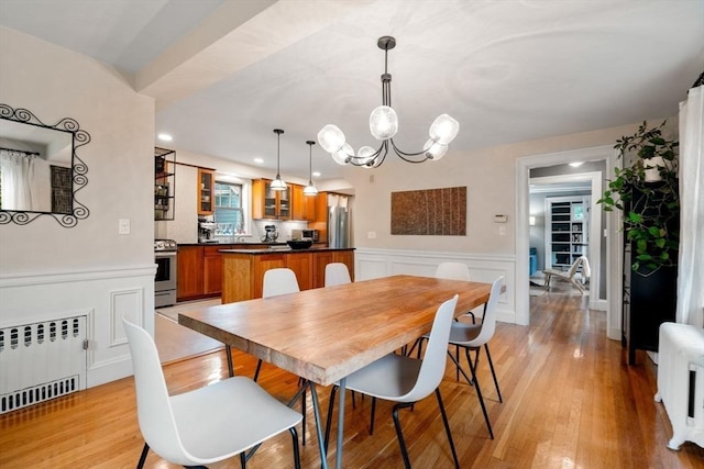 dining room featuring radiator, a wainscoted wall, radiator heating unit, an inviting chandelier, and light wood-type flooring