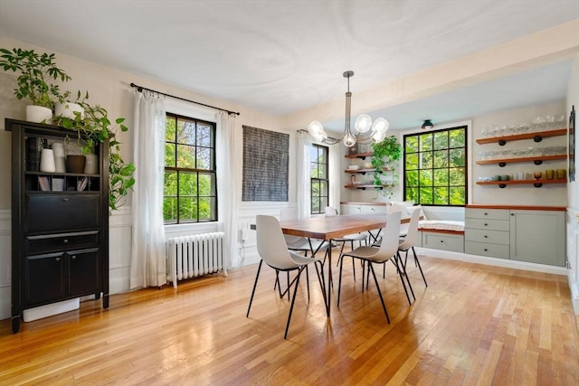 dining room featuring light wood-type flooring, a healthy amount of sunlight, radiator heating unit, and a chandelier