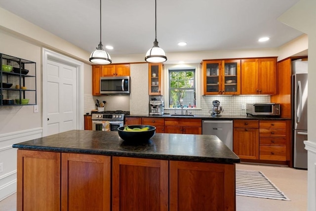 kitchen with stainless steel appliances, a sink, backsplash, brown cabinetry, and dark countertops