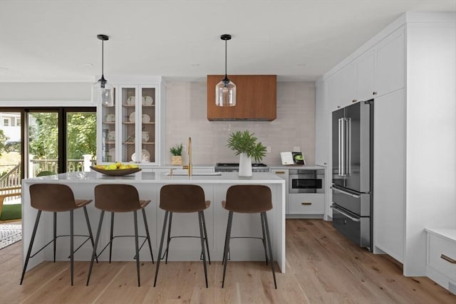 kitchen featuring a kitchen island with sink, white cabinets, a kitchen breakfast bar, hanging light fixtures, and high end fridge