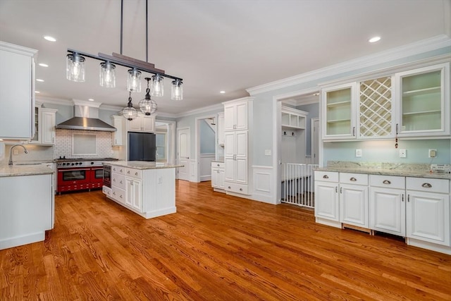 84 Bruce Rd, Concord, MA 01742 - kitchen with wall chimney range hood, black fridge, light wood-style flooring, white cabinets, and crown molding
