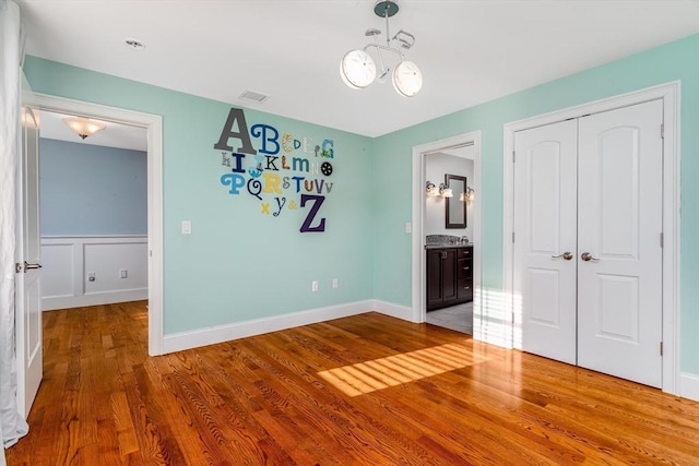 84 Bruce Rd, Concord, MA 01742 - unfurnished bedroom featuring a closet, wood finished floors, a chandelier, connected bathroom, and baseboards
