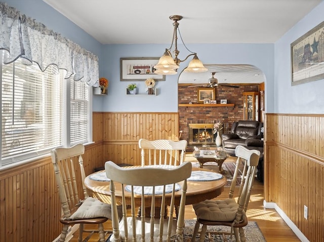 dining area with arched walkways, a ceiling fan, wainscoting, wood walls, and a fireplace