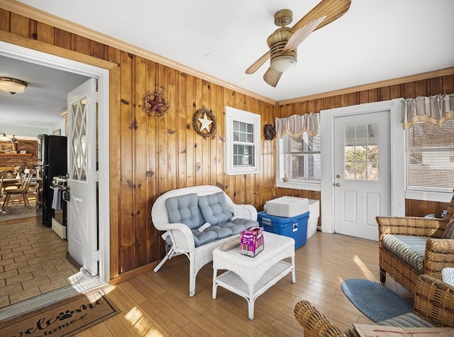 sitting room featuring ceiling fan, wooden walls, crown molding, and hardwood / wood-style floors