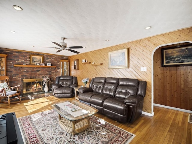 living room featuring visible vents, a ceiling fan, a brick fireplace, baseboards, and hardwood / wood-style flooring