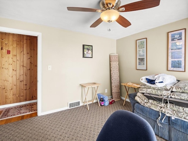 bedroom featuring a ceiling fan, carpet, wooden walls, and baseboards