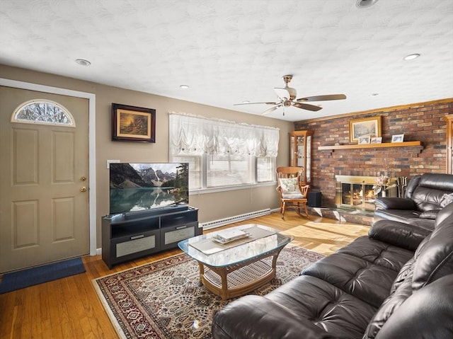 living area with a brick fireplace, baseboards, baseboard heating, and wood finished floors