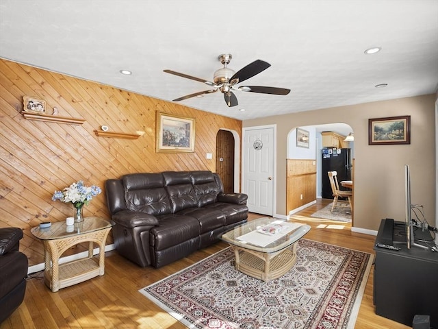 living room with light wood-style floors, arched walkways, and a ceiling fan