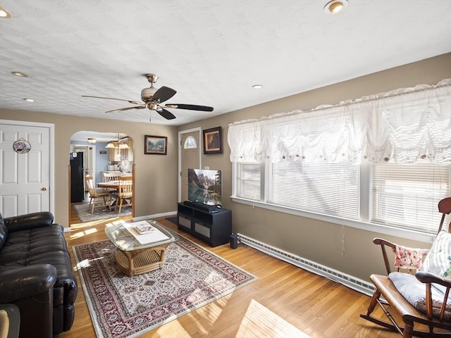 living area featuring arched walkways, a baseboard radiator, baseboards, and wood finished floors