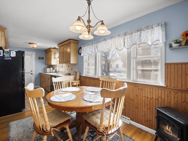 dining room with light wood-style floors, a wainscoted wall, a notable chandelier, and wooden walls