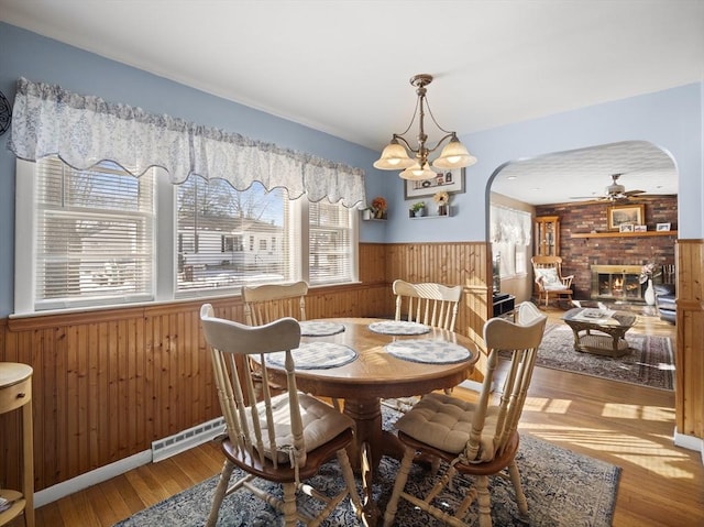 dining area featuring arched walkways, a fireplace, wood-type flooring, wainscoting, and wood walls