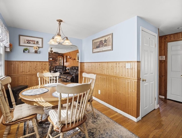 dining space with a wainscoted wall, wood walls, arched walkways, and wood finished floors