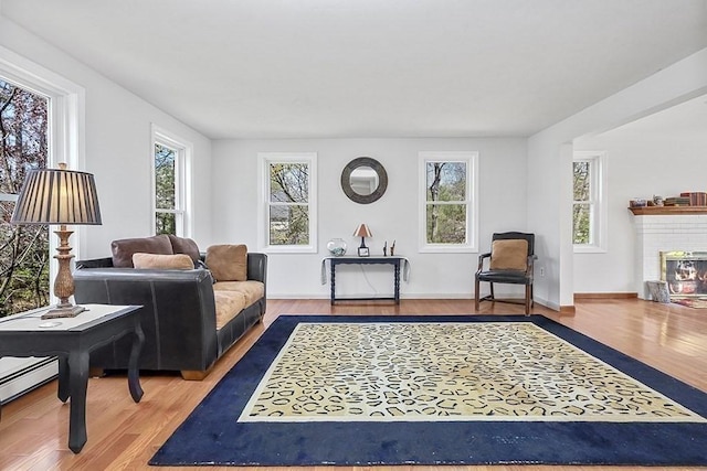 living area with plenty of natural light, a baseboard heating unit, a brick fireplace, and wood finished floors