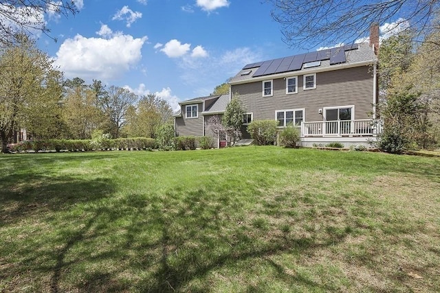 rear view of house featuring roof mounted solar panels, a wooden deck, a yard, and a chimney