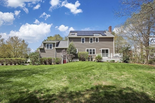 back of property featuring a yard, a chimney, solar panels, and a wooden deck