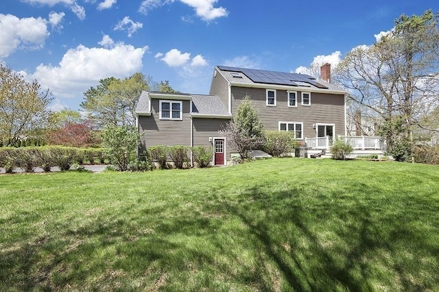 back of house featuring a lawn, roof mounted solar panels, a wooden deck, and a chimney