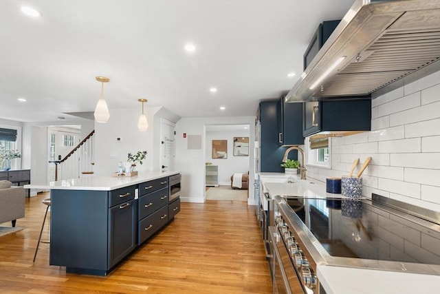 kitchen with light wood-type flooring, a kitchen breakfast bar, wall chimney exhaust hood, range, and open floor plan