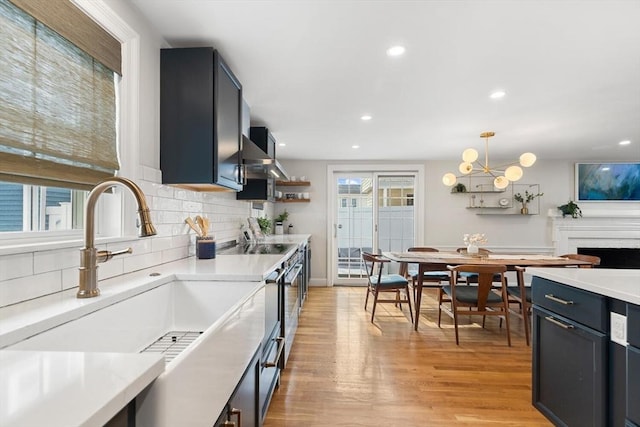 kitchen featuring decorative light fixtures, light countertops, decorative backsplash, light wood-style floors, and a sink