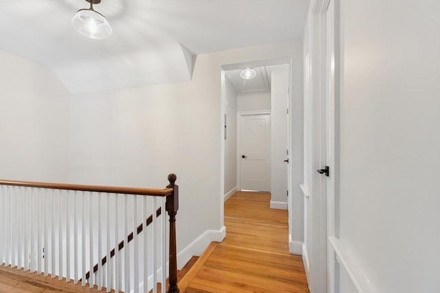 hallway featuring baseboards, attic access, vaulted ceiling, light wood-style floors, and an upstairs landing