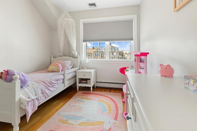 bedroom with baseboard heating, visible vents, and wood finished floors