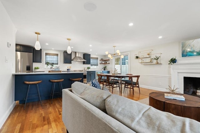 living area with recessed lighting, baseboards, a brick fireplace, and light wood-style flooring