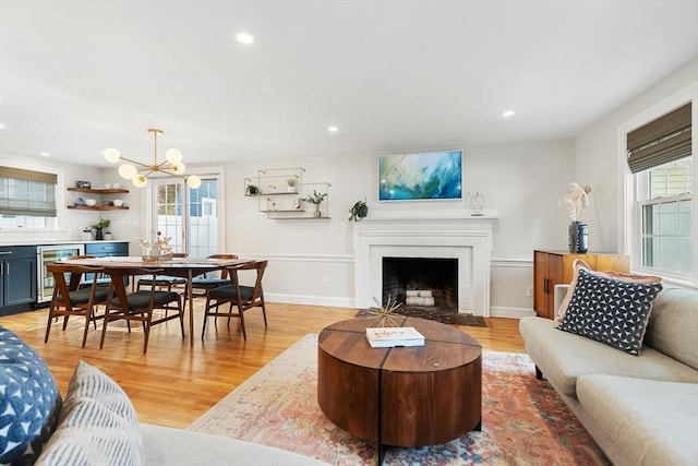 living room with beverage cooler, a fireplace, a wealth of natural light, and light wood-style floors