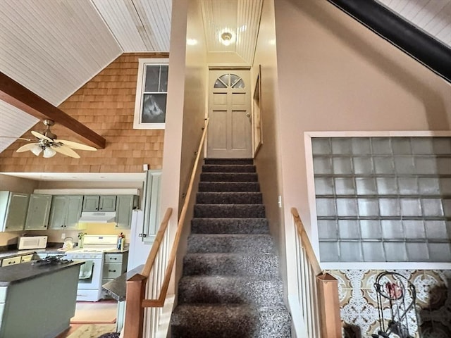 stairs featuring beamed ceiling, ceiling fan, wooden ceiling, and high vaulted ceiling