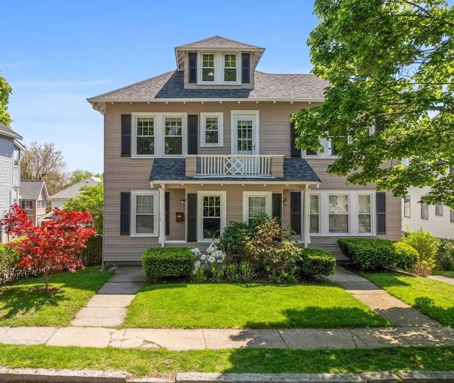 american foursquare style home featuring a front yard and a shingled roof