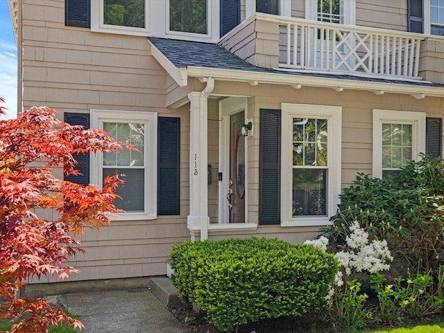 view of exterior entry featuring a balcony and roof with shingles