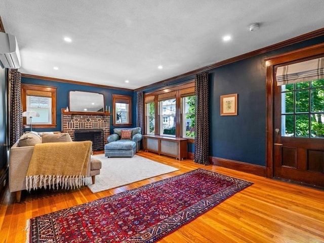 living room with ornamental molding, an AC wall unit, wood finished floors, a brick fireplace, and baseboards