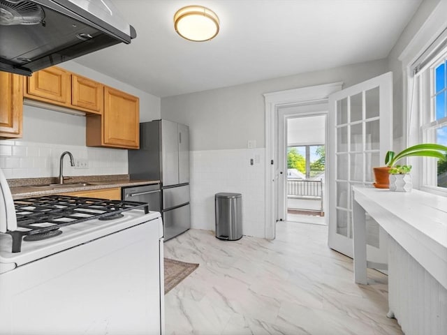 kitchen featuring white range with gas cooktop, a sink, extractor fan, light marble finish flooring, and freestanding refrigerator