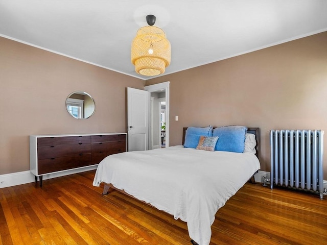 bedroom featuring radiator, wood finished floors, crown molding, and baseboards
