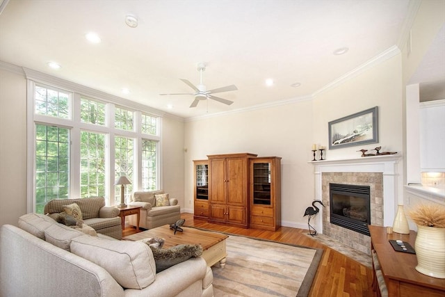 living area featuring a tiled fireplace, baseboards, light wood-style floors, and ornamental molding