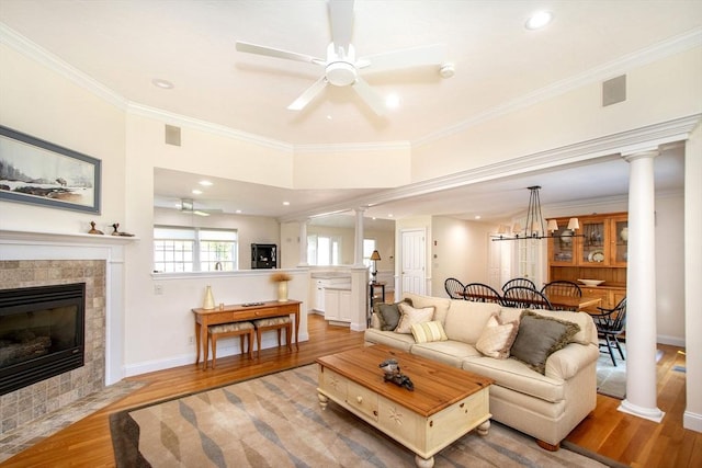 living room featuring light wood finished floors, a tile fireplace, ornate columns, and ornamental molding