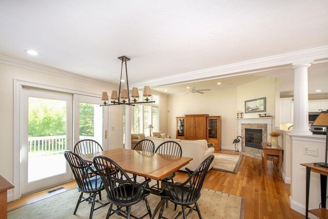 dining space with visible vents, light wood finished floors, decorative columns, a fireplace, and crown molding