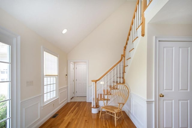 foyer entrance with visible vents, a wainscoted wall, stairs, lofted ceiling, and wood finished floors