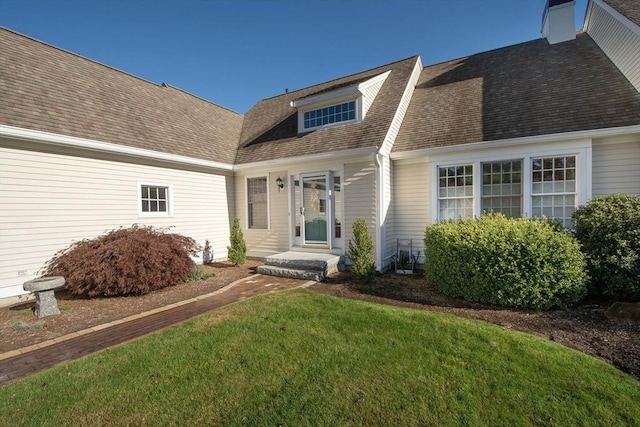 property entrance featuring a lawn, a chimney, and roof with shingles