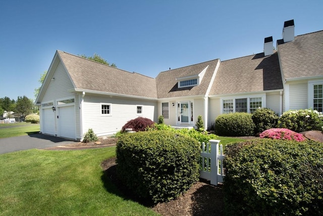 view of front of house with aphalt driveway, an attached garage, a front yard, and roof with shingles