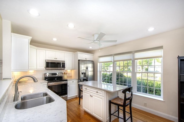 kitchen featuring light stone countertops, light wood finished floors, a sink, stainless steel appliances, and backsplash