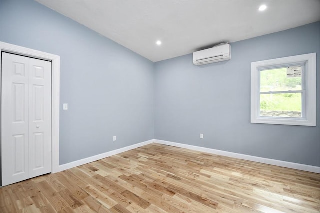 empty room with light wood-type flooring, a wall mounted air conditioner, recessed lighting, and baseboards