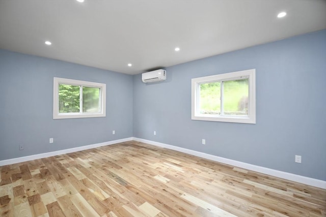 unfurnished room featuring a wealth of natural light, light wood-type flooring, an AC wall unit, and baseboards