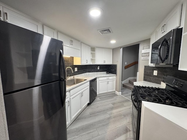 kitchen with sink, white cabinetry, black appliances, light wood-type flooring, and backsplash