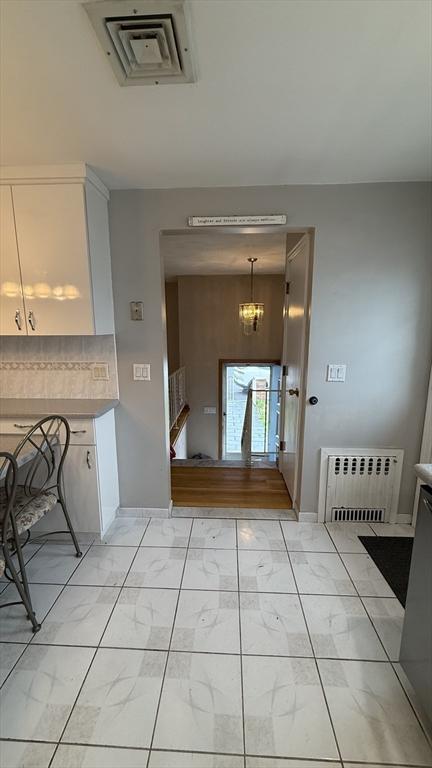 unfurnished dining area featuring light marble finish floors, a chandelier, radiator, and baseboards